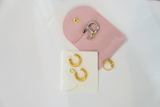 Aros de oro y plata en negrita y anillo de oro con bolsos de joyería blancos rosados y crema sobre un fondo blanco - Foto, imagen