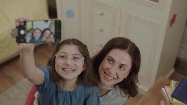 Little cute girl taking selfie with her young mother, recording video, photographing beautiful moment. Mother looking at camera while enjoying daughter video call. Front phone camera view. - Záběry, video