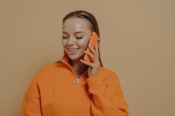 Isolated studio shot of happy smiling woman talking on mobile phone with best friend or family member, sharing last news via cellphone, female enjoying pleasant fun call conversation - Valokuva, kuva