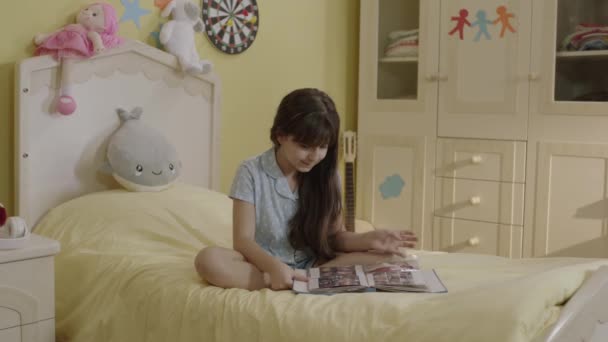 Mother giving a birthday present to her daughter sitting on her bed in her room. Young mother closes her daughter's eyes and waits to show a surprise gift. The cute girl is happy to see the gift. - Video, Çekim