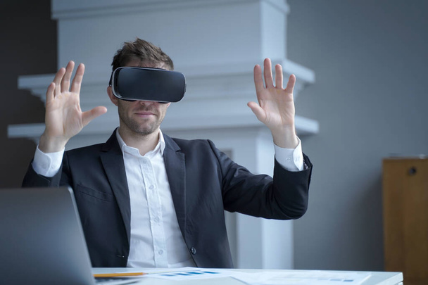 Businessman using technology of augmented reality at home office work. Man CEO in virtual reality glasses with hands up in air. Focused entrepreneur in electronics 3D goggles interacts with simulation - Photo, Image