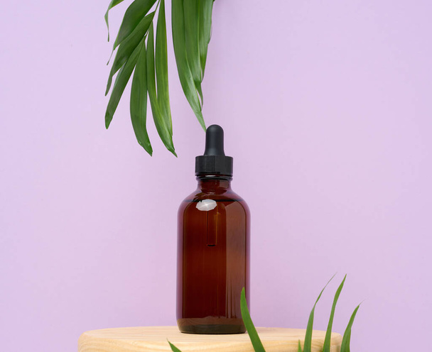 Una bottiglia di vetro marrone con una pipetta su sfondo viola. Contenitori per cosmetici, oli, sieri - Foto, immagini