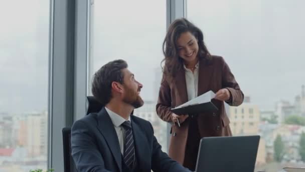 Smiling bearded business man working with attractive secretary in company luxury office. Confident ceo manager sitting desk using laptop. Happy brunette woman assistant holding business documents. - Footage, Video