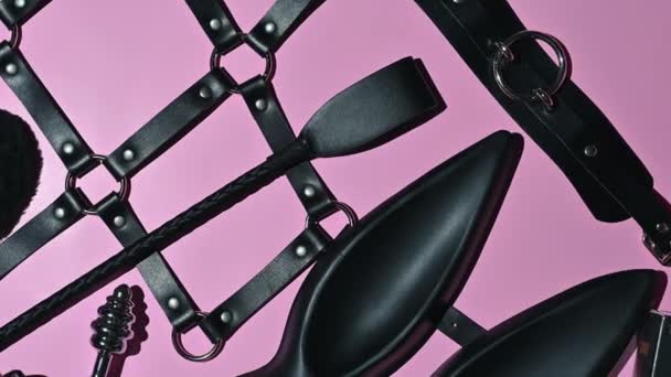 set of adult erotic toys for BDSM sex with submission and domination. Leather flogger whip, handcuffs, mask on pink background - Footage, Video