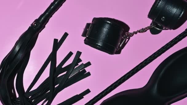 set of adult erotic toys for BDSM sex with submission and domination. Leather flogger whip, handcuffs, mask on pink background - Imágenes, Vídeo