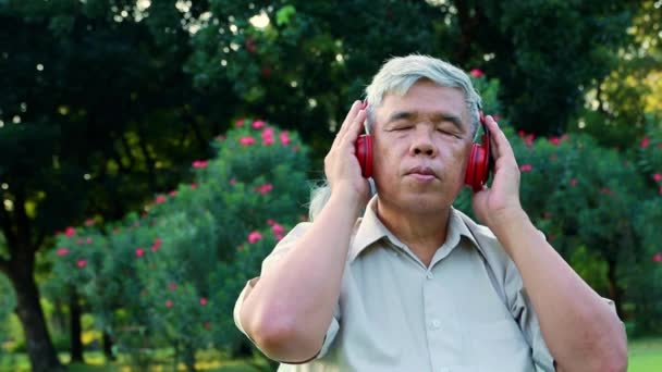 Asiatischer älterer Herr hört unterhaltsame Musik mit Kopfhörern im Garten Freizeitaktivitäten entspannen Gartenbesuch am Abend: Gesundheitsfürsorge, Lebensversicherung für Rentner - Filmmaterial, Video