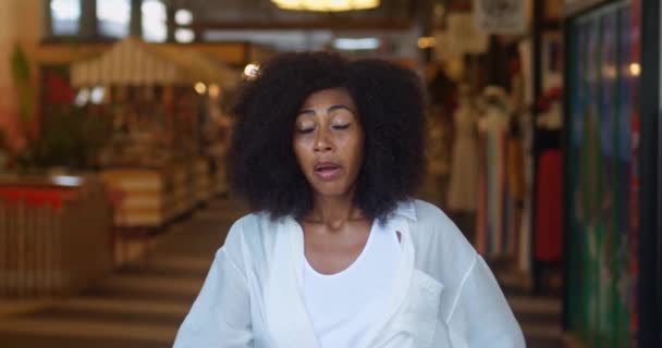 Ogłuszona mieszana kobieta rasy z włosami, kładzie rękę na czole, patrząc na boki z wstrząśniętym wyglądem - Materiał filmowy, wideo