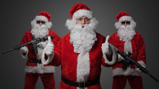 Portret trzech Mikołajów ubranych w czerwony kostium i dwóch ze strzelbami Mikołaja. - Zdjęcie, obraz
