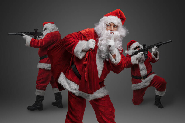 Снимок сумки Санты с рождественскими подарками вокруг двух Санта-Клаусов с винтовками. - Фото, изображение