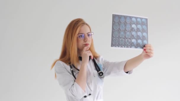 une jeune femme aux cheveux roux étudie les images de tomographie sur fond blanc - Séquence, vidéo
