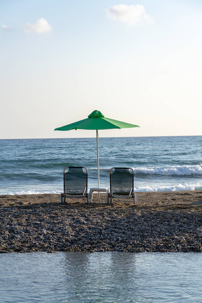 Sedie sdraio sotto gli ombrelloni sulla penisola sabbiosa tra mare e fiume vicino a Georgioupoli, Creta, soleggiata giornata estiva all'alba, concetto di relax, cielo azzurro copia spazio - Foto, immagini