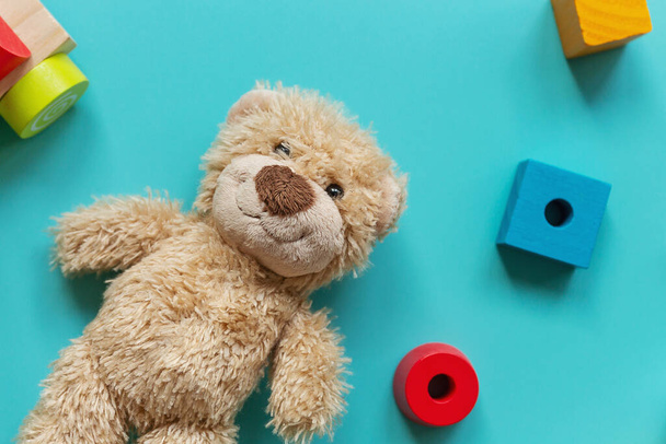 Teddy beer, houten speelgoed, blokken voor kleuters op een blauwe achtergrond. Speelgoed voor kleuterschool, kleuterschool of kinderopvang. Kopieer ruimte voor tekst. Bovenaanzicht, close up - Foto, afbeelding