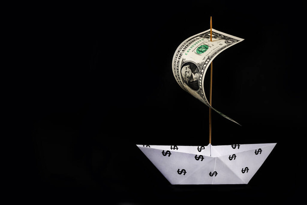 Barco de papel con el símbolo del dólar americano y una vela hecha de un billete de 1 dólar - Foto, imagen