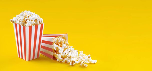 Two red white striped carton buckets with tasty cheese popcorn, isolated on yellow background. Box with scattering of popcorn grains. Movies, cinema and entertainment concept. - Photo, Image