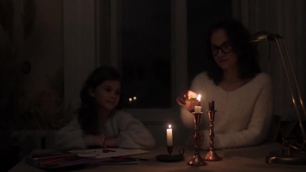 Maman dans l'obscurité allume des bougies dans une pièce sombre en raison d'une panne de courant afin que sa fille puisse voir ses livres à colorier. - Séquence, vidéo