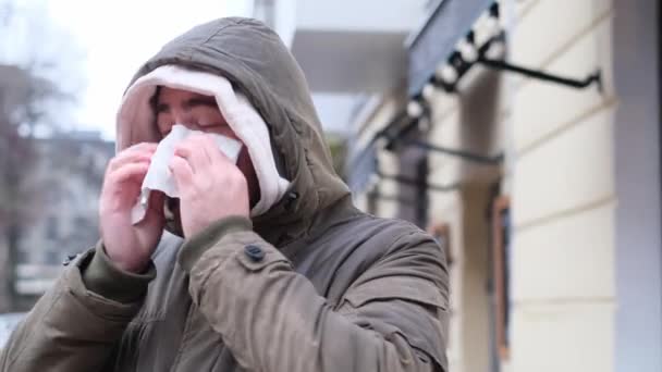 Um rapaz doente espirra no meio da rua, à chuva. Um tipo não saudável com sintomas de gripe. Conceito pandêmico. 4k vídeo - Filmagem, Vídeo