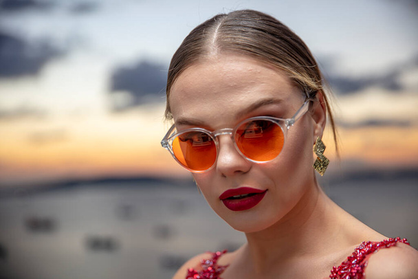 Gyönyörű női modell színes szemüveget visel naplementekor. Szabadtéri romantikus portré vonzó szőke nő smink és szemüveg pózol. Isztambul szigetcsoport (Princess-szigetek) városképe. - Fotó, kép