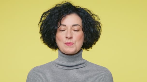 Snoepbel concept met kopieerruimte, slow motion. close-up gelukkig speelse volwassen vrouw in de 40 met korte krullend kapsel blazen bel van kauwgom op camera over pastel gele achtergrond in studio - Video