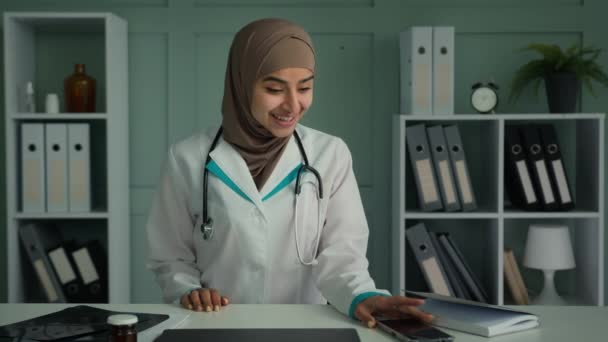 ポートレート幸せな医師イスラム教徒の女性でヒジャーブ女性医師婦人科若い世代のアラビア民族学生は、医療インターンシップの終わりを祝う携帯電話のダンスのお祝いに良い通知を読みます - 映像、動画