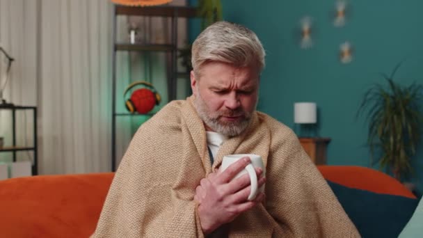 Ekoseye sarılı hasta bir adam kanepede soğuktan titreyerek oturur, ısınmamış bir dairede ısıtmadan sıcak çay içer. Sağlıksız, kendini rahatsız hisseden olgun bir adam akşam evde ısınmaya çalışır. - Video, Çekim