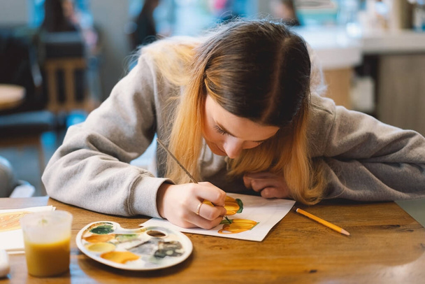Jolie adolescente dessine un tableau avec de la peinture d'affiche. Vue de face d'un dessin d'une fille avec une palette à la main. Une jeune adolescente souriante dessine un tableau - Photo, image