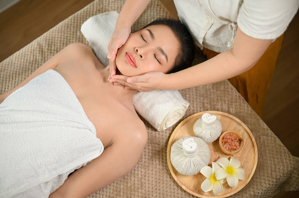 Calme et détendu jeune femme asiatique ayant massage du visage ou un traitement du visage au salon de beauté spa. vue ci-dessus - Photo, image