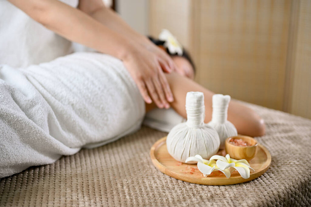 Tajska koncepcja spa, kulki ziołowe Spa lub znaczki do masażu i sól spa na stole do masażu z młodą damą otrzymującą masaż na stole do masażu. - Zdjęcie, obraz