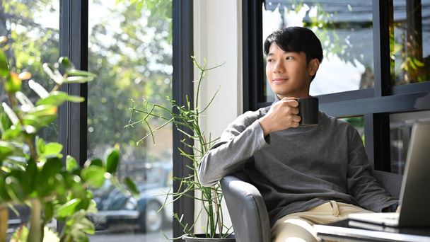 Chytrý mladý asijský samec na volné noze nebo podnikatel popíjení kávy, chlazení při vzdálené práci v kavárně. - Fotografie, Obrázek