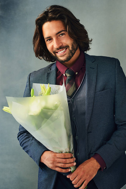 Fancy some romance. Studio portrait of a stylishly dressed handsome young man smiling and holding a bouquet of flowers - Photo, image