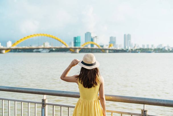 ダナン市を訪れる黄色のドレスを着た女性旅行者。ドラゴンブリッジで川の景色を観光。ランドマークと観光名所に人気があります。ベトナムと東南アジア旅行のコンセプト - 写真・画像