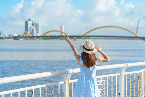 Da Nang şehrinde gezen mavi elbiseli bir kadın. Dragon Köprüsü ile nehir manzarasını gezen turistler. Şehir simgesi ve turistik ilgi odağı. Vietnam ve Güneydoğu Asya seyahat kavramı - Fotoğraf, Görsel