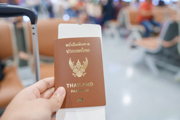 Hand holding Thailand passport and boarding pass ticket in International airport. Travel, vacation and transportation concepts - Photo, Image