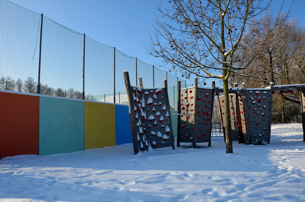 αναρρίχηση τοίχο στην παιδική χαρά στο πάρκο. στερεά δοκάρια με λαβές αναρρίχησης σε μορφή χρωματισμένων λίθων από σύνθετο υλικό για λιθοδομή, προεξοχή, γέφυρα, σήραγγα, γαλάζιο ουρανό - Φωτογραφία, εικόνα