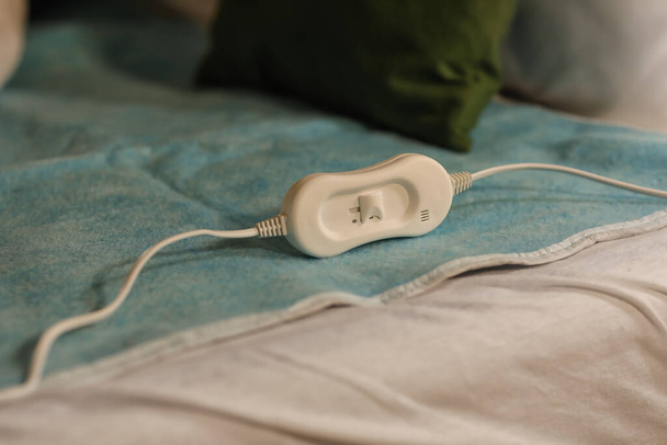 Elektryczna podkładka grzewcza z regulatorem na łóżku w nocy, zbliżenie - Zdjęcie, obraz