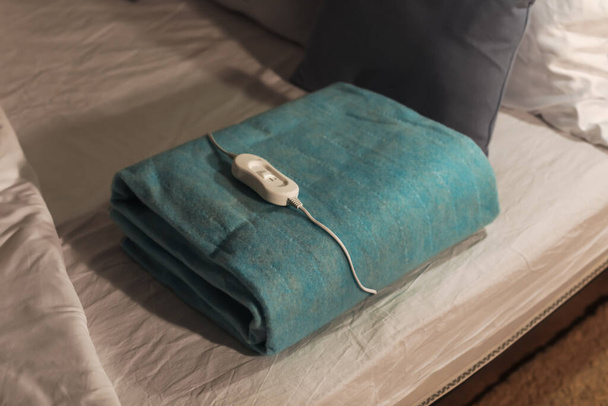 Składana elektryczna podkładka grzewcza z regulatorem na łóżku w nocy, zbliżenie - Zdjęcie, obraz