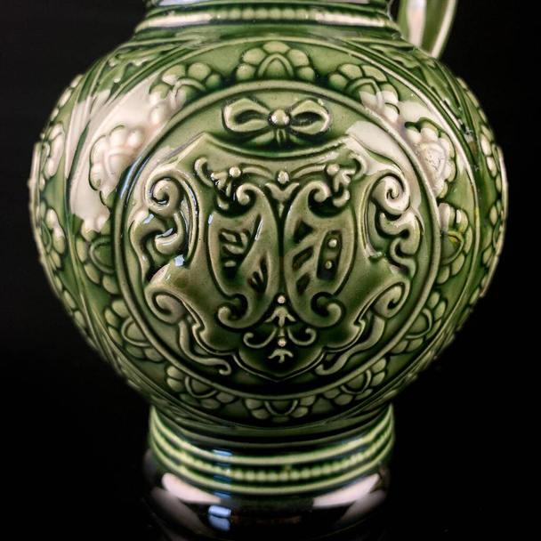 antique green ceramic jug with national patterns. vintage jug with an ornament on a black isolated background - Photo, Image