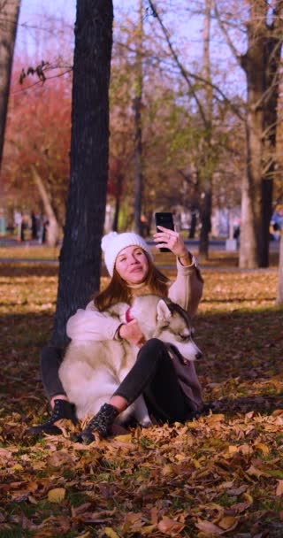 Egy fiatal nő online videóhívás közben, miközben átöleli a husky-ját. Modern trendek a közösségi hálózatokban és az állatok iránti szeretet. Lassú mozgás 4k felvétel. - Felvétel, videó