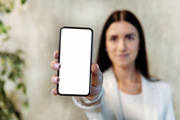 Lágy fókusz a fiatal női vállalkozó bemutató mobiltelefon üres képernyőn a kamera munka közben az irodában - Fotó, kép