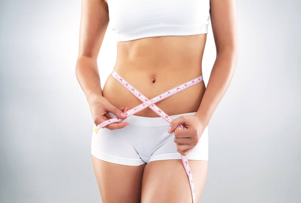 Слегка похудел. Студийный снимок неузнаваемой девушки, измеряющей свою талию на сером фоне - Фото, изображение