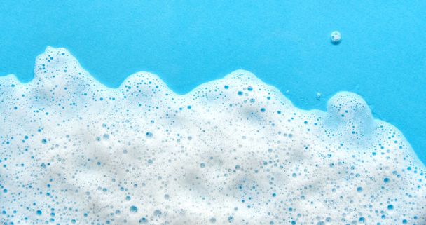 White foam soap sud on blue background. Foam bubbles of detergent fluid gel. - Photo, Image
