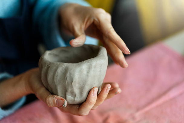 Womens hands knead the clay and sculpt a cup from it. The process of manufacturing a ceramic product,close up. - Photo, Image