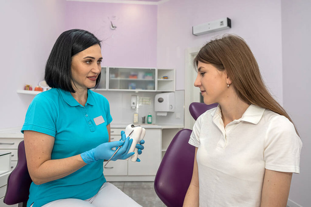 Portret van een gelukkige patiënt met gezonde tanden zittend in een tandartsstoel naast een jonge vrouwelijke tandarts. onderzoek van de patiënt. Raadpleging in een tandheelkundige kliniek - Foto, afbeelding
