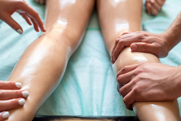 Zwei Massagetherapeutinnen, eine Frau und eine Ma, geben einem Mädchen in einem Wellness-Salon eine doppelte Fuß- und Beinmassage. Vier hände von masseur während massage close up - Foto, Bild