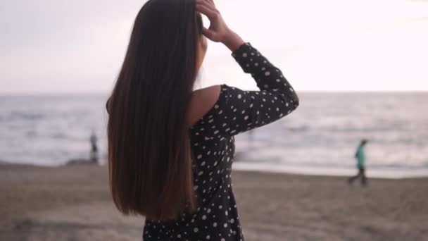 Een mooie brunette past haar lange donkere haar aan, strand bij zonsondergang. Langzame beweging - Video
