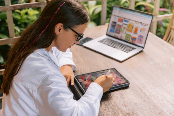 Atraktivní mladá žena návrhářka pomocí digitálního tabletu a notebooku v letní kanceláři - Fotografie, Obrázek