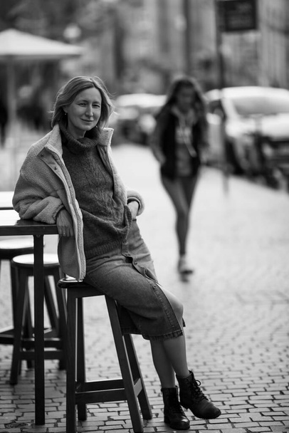 Nainen istuu tuolilla Portugalin jalkakäytäväkahvilan ulkopuolella. Musta ja valkoinen kuva. - Valokuva, kuva