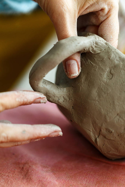Las manos de las mujeres amasan la arcilla y esculpen una taza de ella. El proceso de fabricación de un producto cerámico, de cerca. - Foto, Imagen