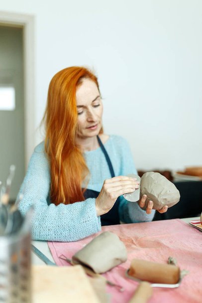 Estudio de cerámica, negocio artesanal, pelo rojo alfarero femenino sosteniendo tazón de cerámica listo para la cocción en un horno. - Foto, imagen
