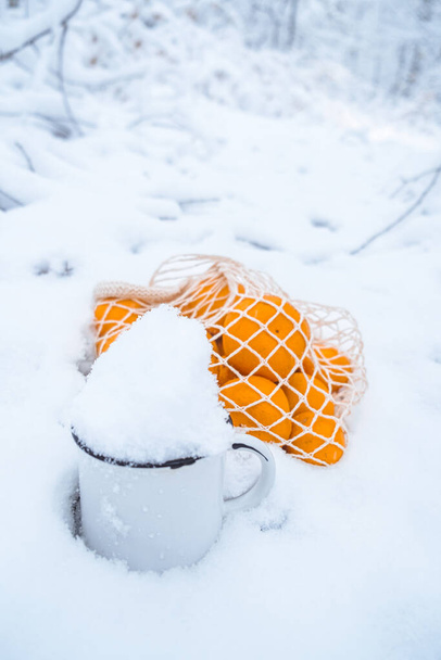 besneeuwd landschap rieten zak gevuld met mandarijnen en kopje sneeuw - Foto, afbeelding