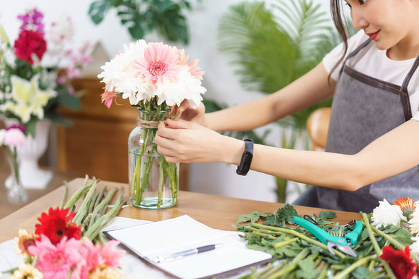 Flower shop concept, Vrouwelijke bloemist is het versieren van kleurrijke bloemen vaas door hennep touw in boog vorm. - Foto, afbeelding